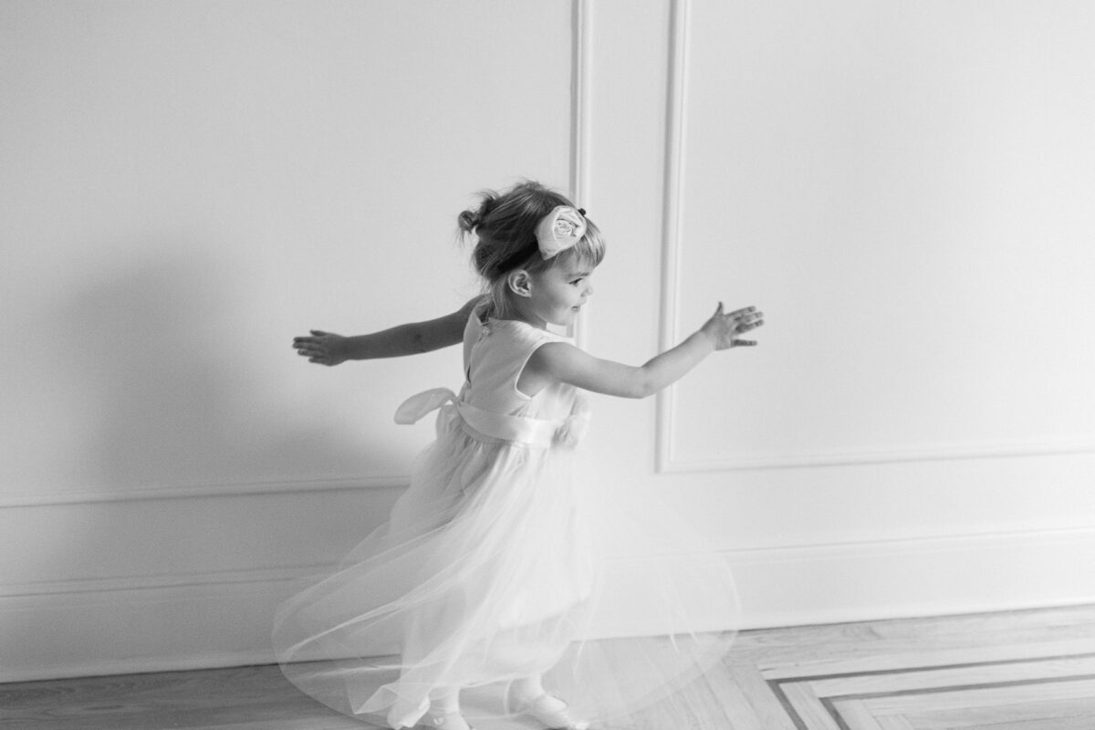 Une petite fille vêtue d'une jolie robe blanche tourne sur elle-même. Petite bouquetière de mariage.