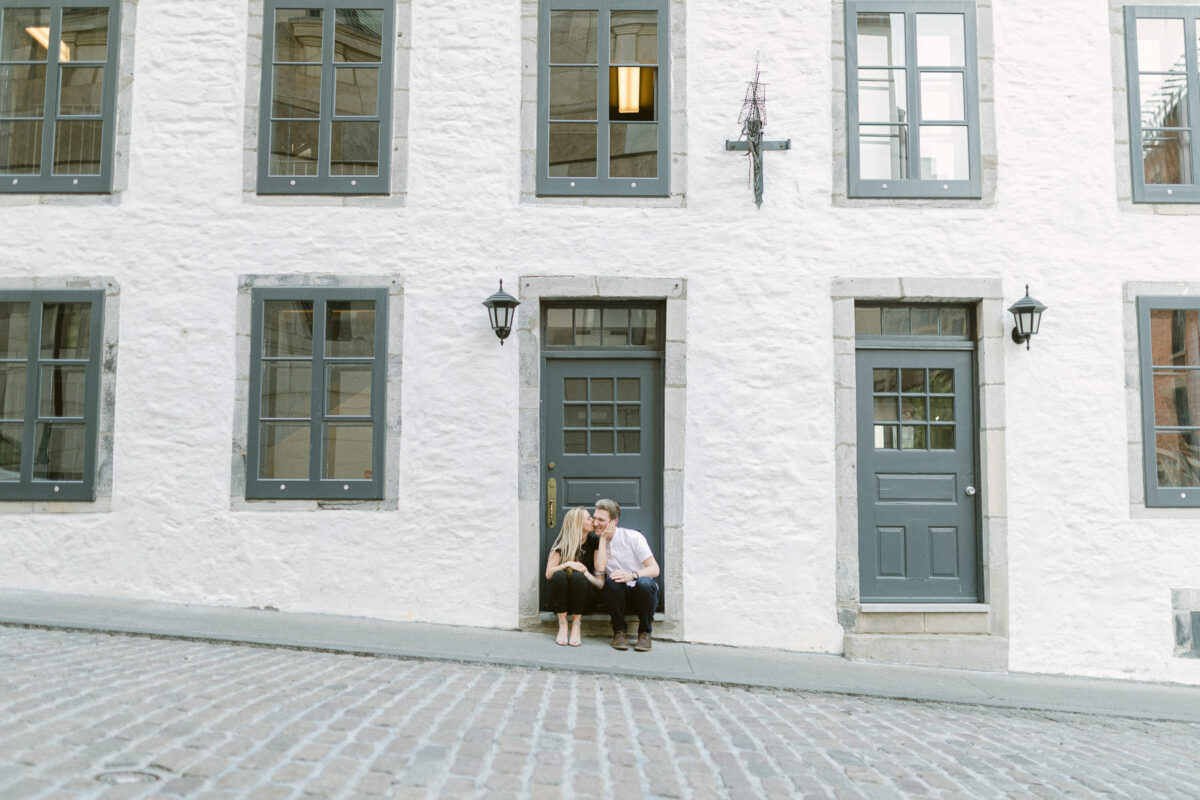 Photo de couple au Vieux Montréal. Les amoureux devant un immeuble en brique blanche.