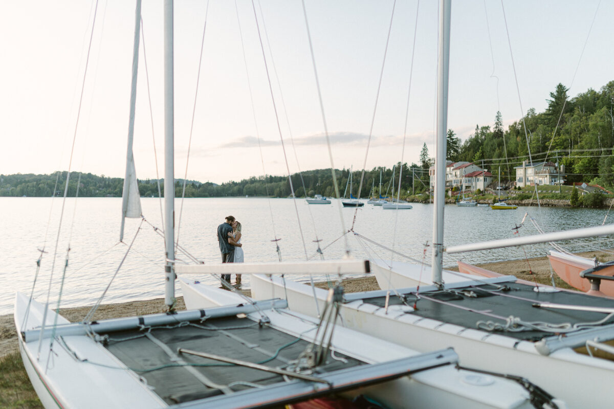 Séance photo en amoureux près d'un lac et catamarans au coucher du soleil.