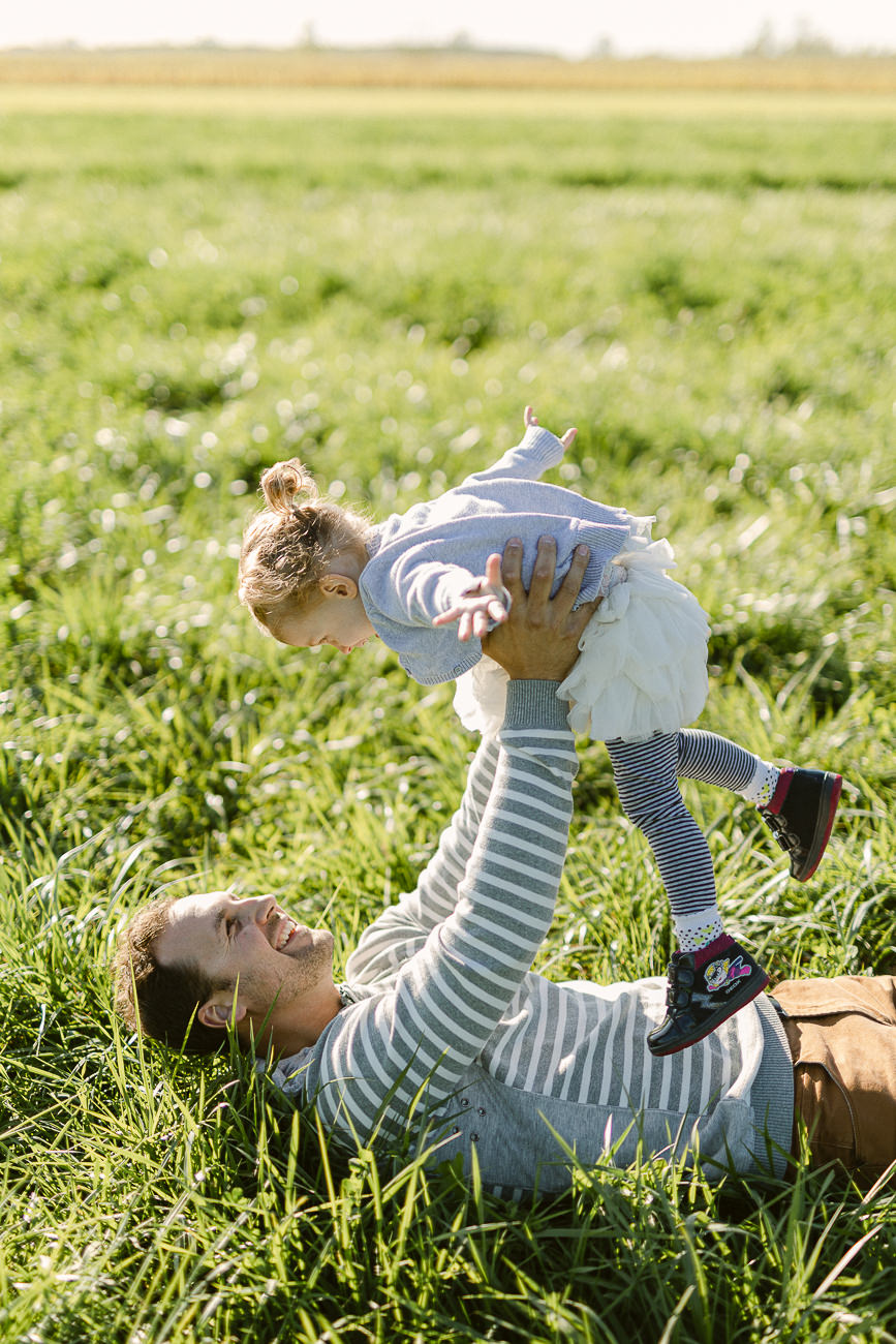 Un papa et sa petite fille s'amusent dans l'herbe haute d'un champs. Séance photo lifestyle.