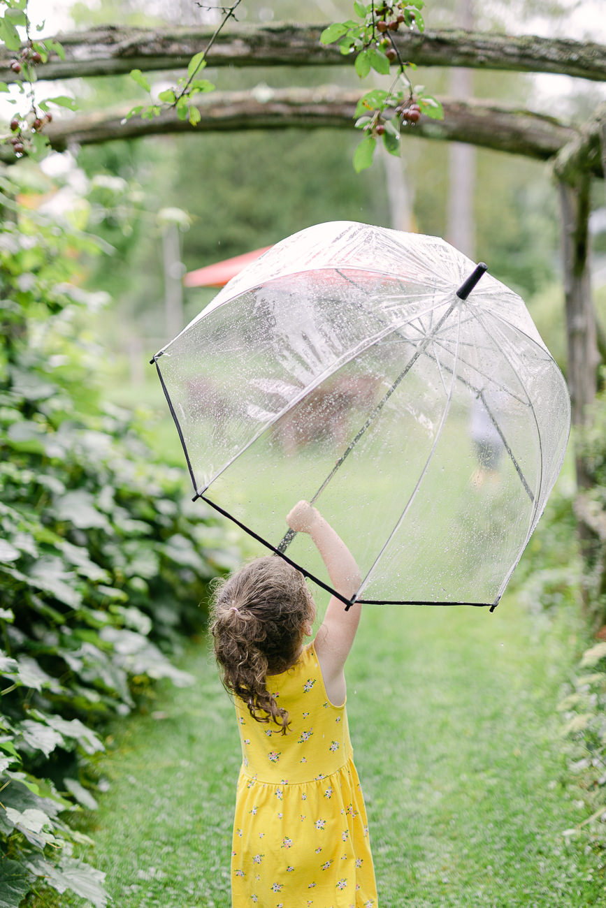 Une petite fille sous la pluie qui tient un parapluie.