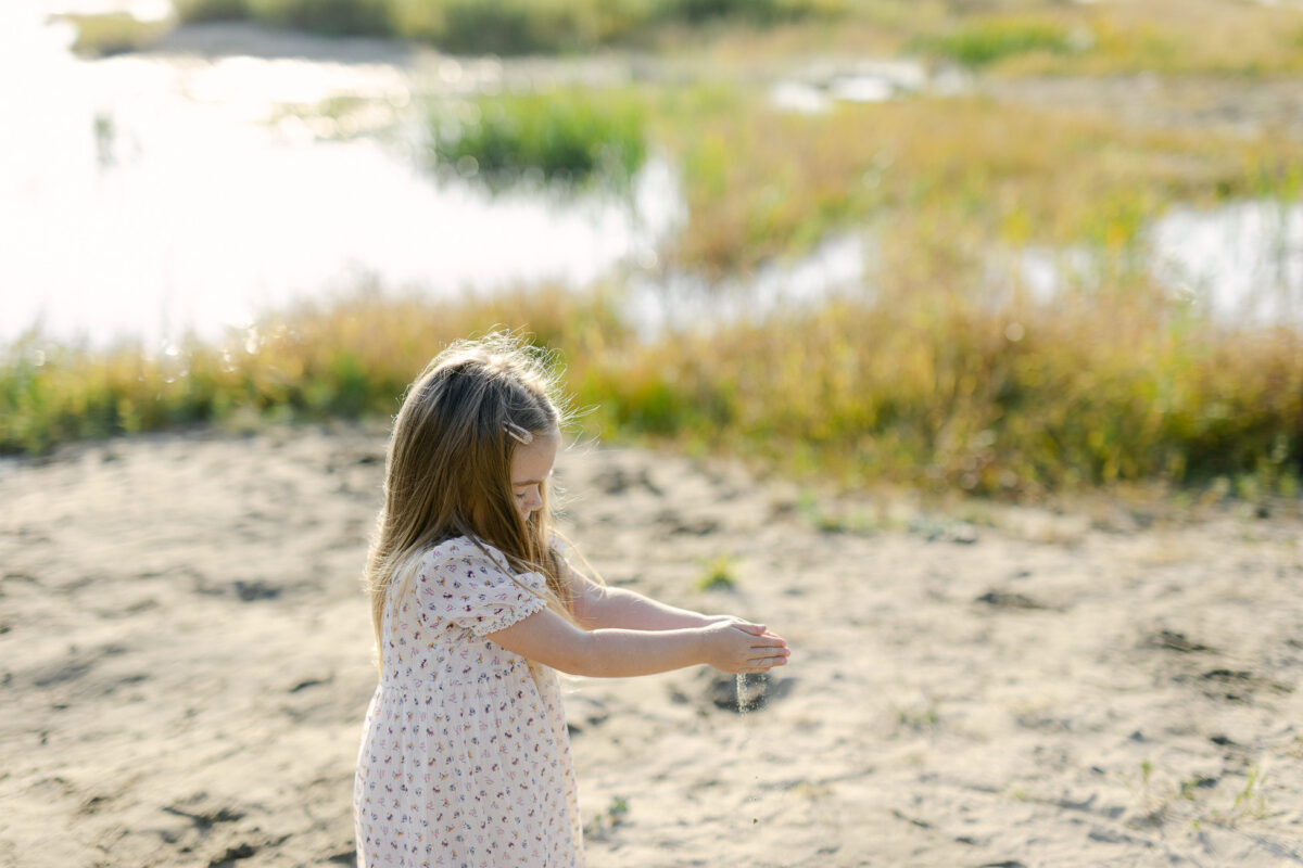 Une petite fille joue avec le sable sur une plage ensoleillée.